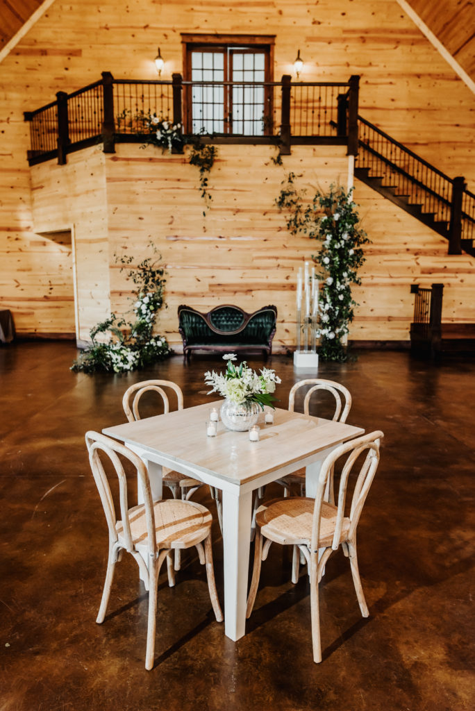 Square wood cocktail table paired with bentwood chairs, velvet green loveseat with green & white floral scape inside The Carolina Barn at McCormick Farms