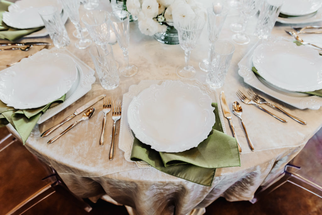Velvet linen crystal glass stemware with modern silverware.  ghost chair at round table.  sage green napkin. The Carolina Barn at McCormick Farms
