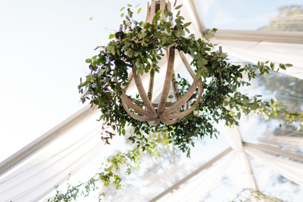 wooden chandelier with greenery hanging in clear top tent