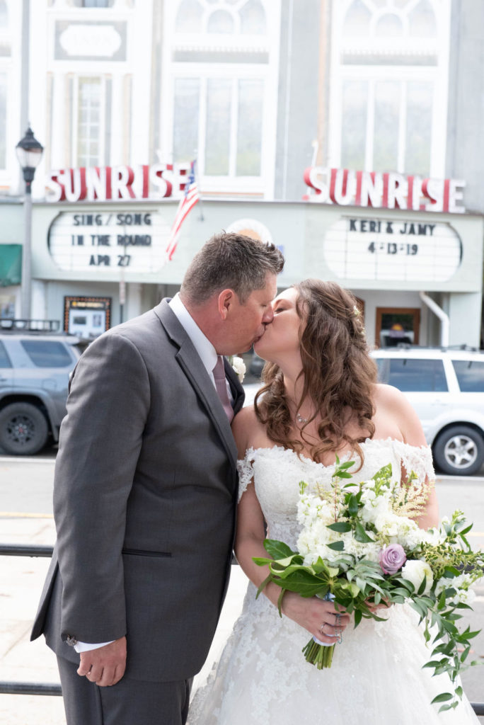 bride and groom kissing in front of theatre sign